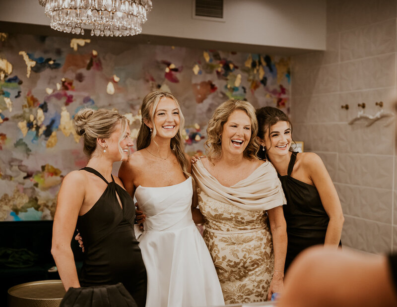 Bride with her mother and bridesmaids smiling in the mirror