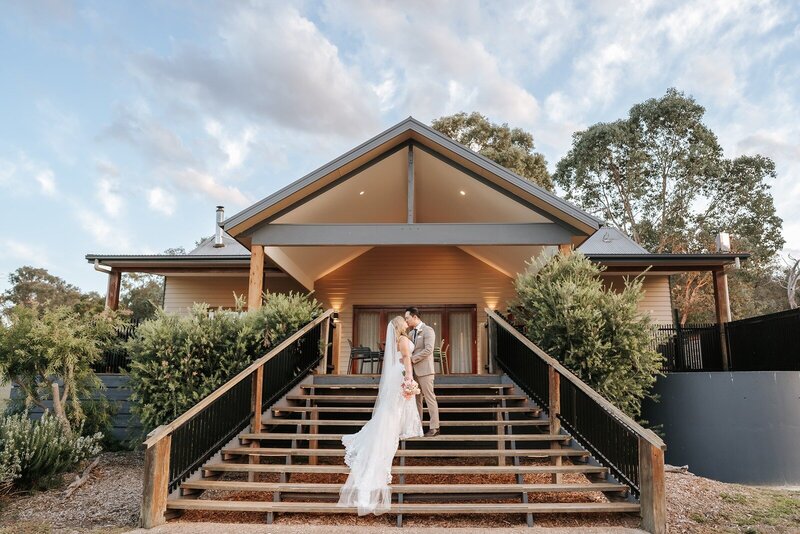 A bride and a groom kissing on the steps of a cottage.