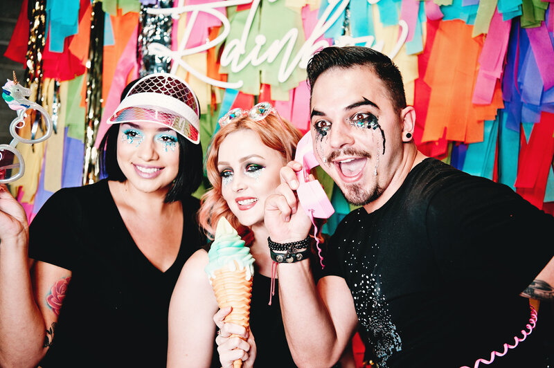Three guests posing with fun props and colorful accessories in front of a rainbow fringe backdrop, captured in a looping moment by MISGIF’s animated GIF photo booth at a corporate event in Phoenix, Arizona