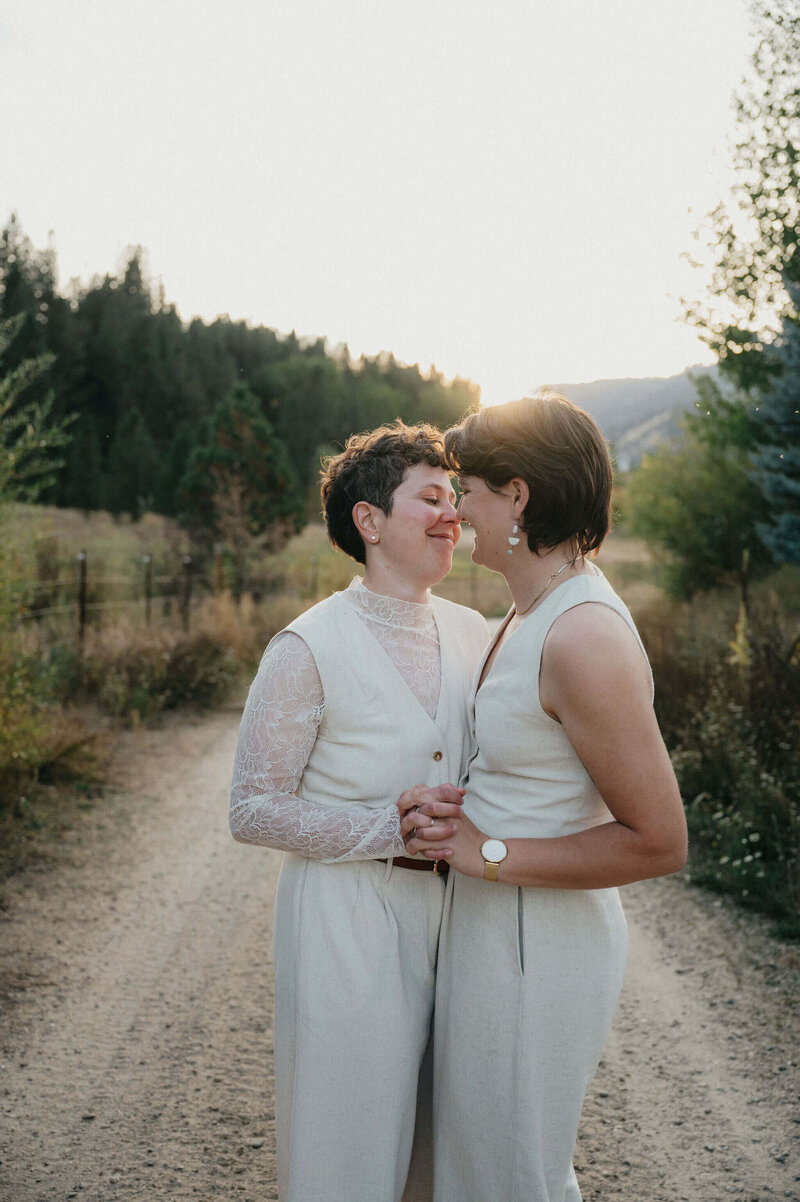 A couple holds hands and leans forward to kiss on a dirt road at their intimate wedding in Boise.