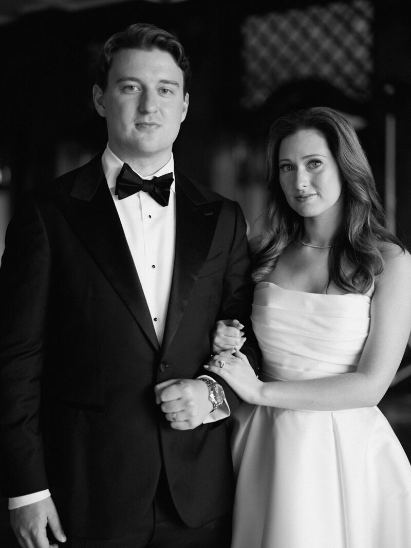 Black and white wedding portrait of a bride and groom standing together in an elegant, timeless setting.