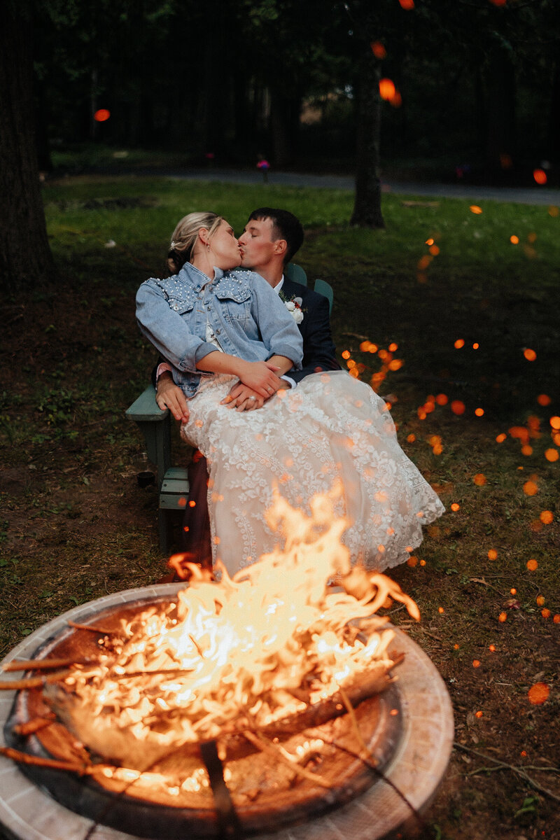bride and groom kissing while sitting in front of a bonfire