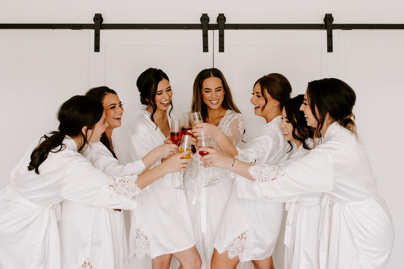 Bride and bridesmaids cheers to one another as they get ready.