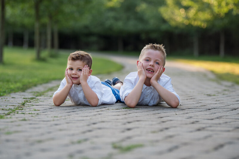 Two boys with laying down on the ground with their hands on their face being silly at their family photoshoot.