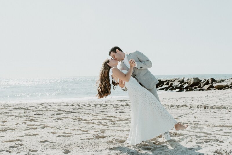 Groom dipping and kissing bride on beach in California