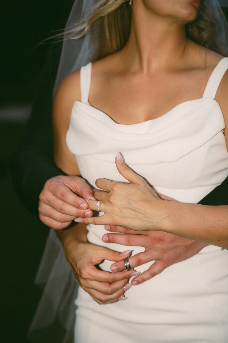 Bride and groom place wedding rings on each other's fingers as they embrace