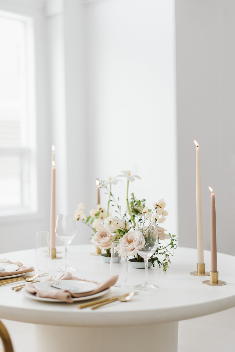 Intimate table setting for two with 3 lit nude candles and a floral centerpiece