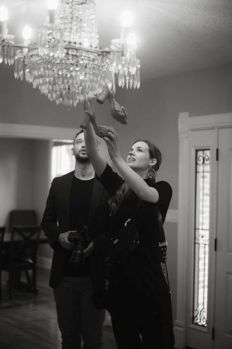 Black and white photo of Stephen and Kaity from Rainstorm Photo & Video setting up a creative wedding shot under a chandelier, capturing the preparation and artistry behind the scenes.
