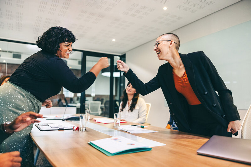 Two colleagues bump fists over a conference table.