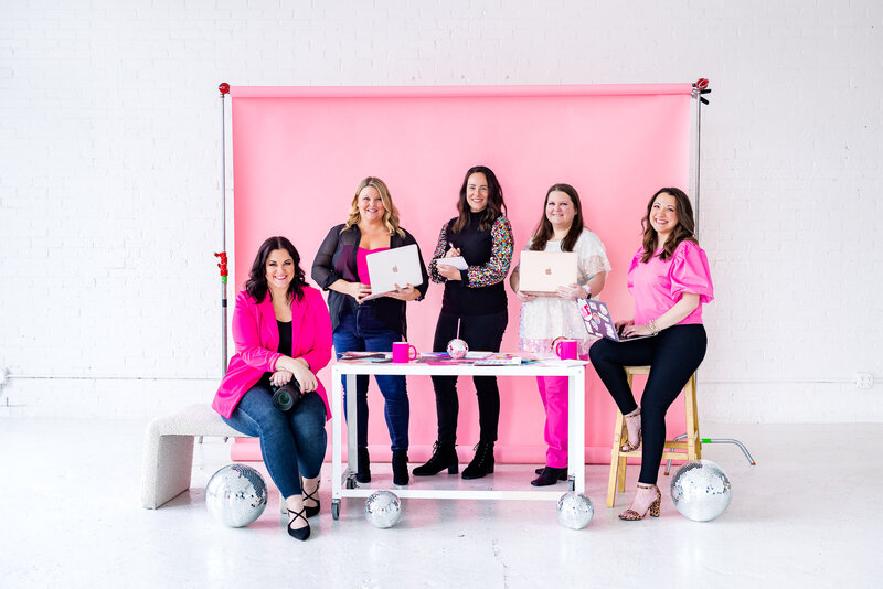 This Way to Fabulous Team - 5 women around a white table with a pink background. Some of them holding their laptops posing for the camera