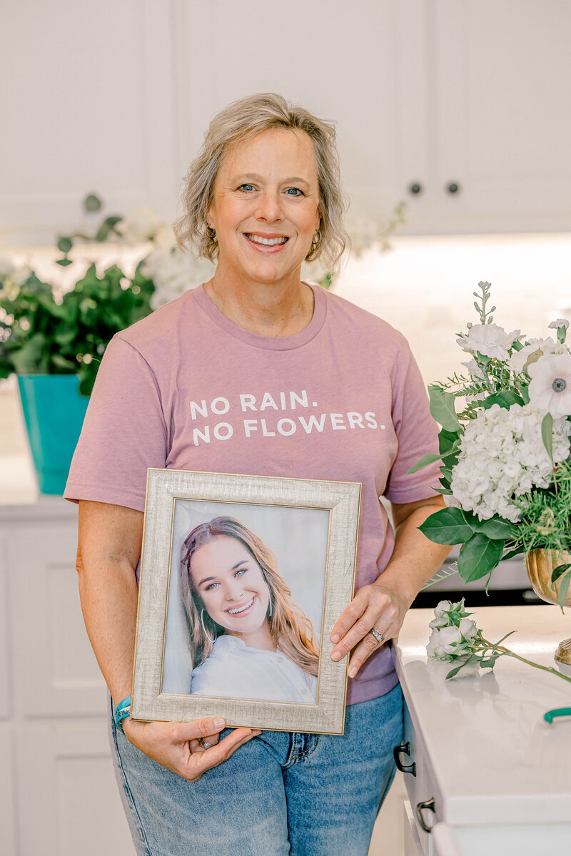 Blonde woman in lavender tea shirt holding picture frame of dark haired girl