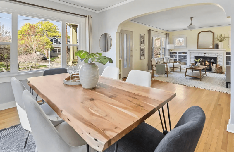 A dining room featuring a large wooden table and a look into the living room.
