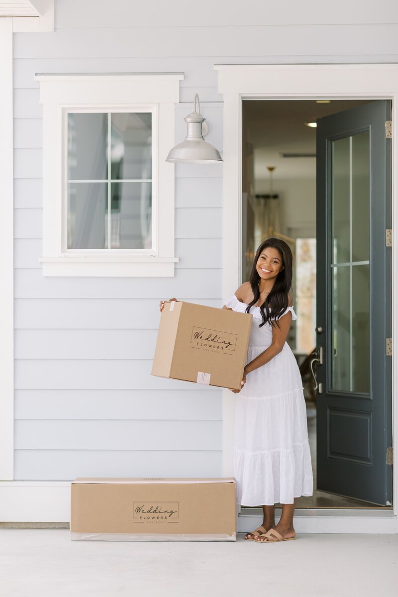 Girl carrying a box into a house for a brand shoot representing wedding flowers for rent in Charleston, south carolina.