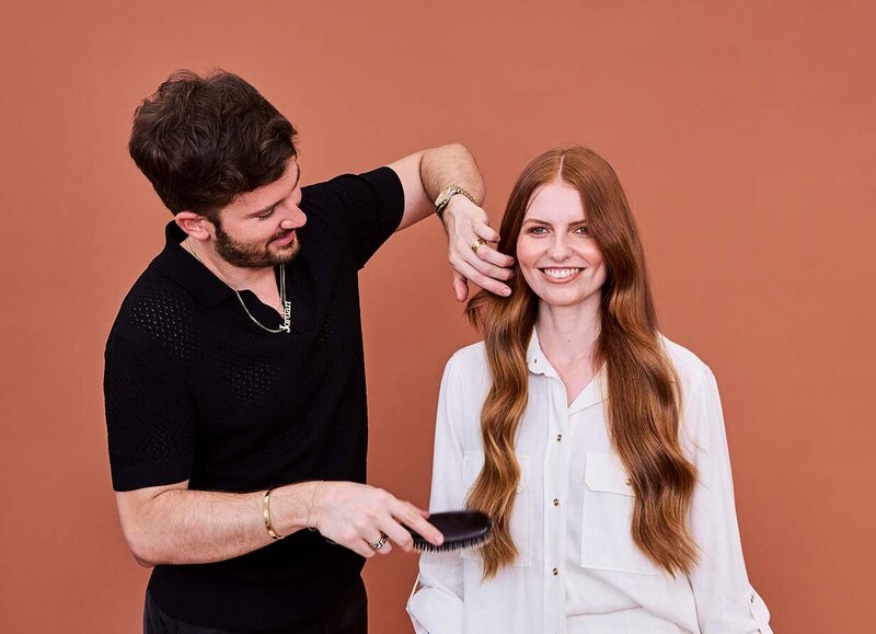 Hairdresser styling long, wavy red hair with a brush, showcasing professional ladies' haircut techniques.