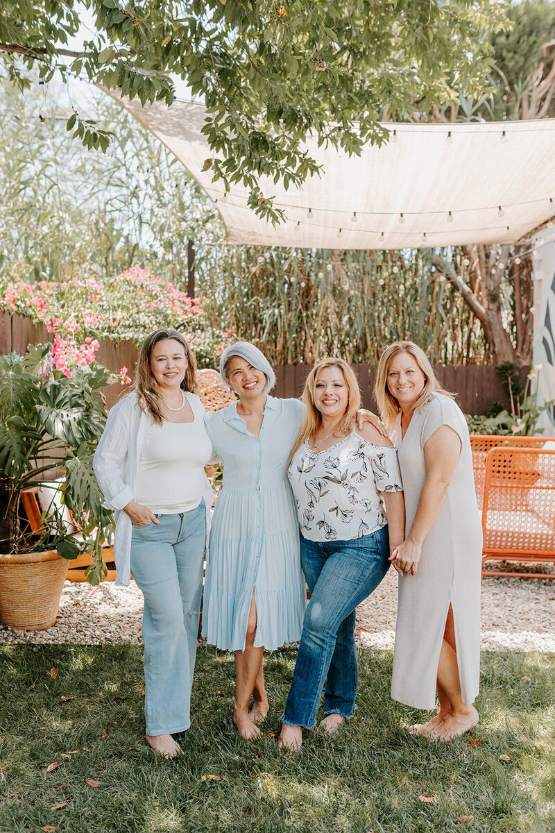 Four women in midlfe standing in a garden with smiling faces.