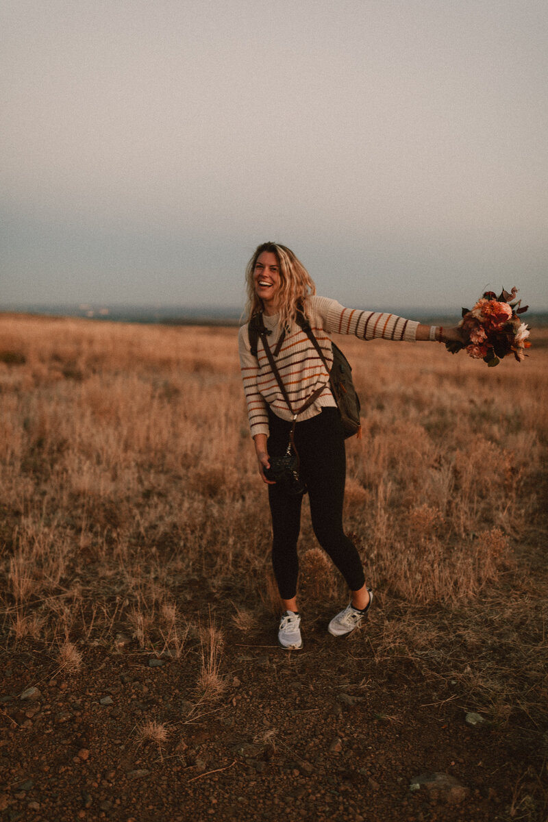 Owner of Wild Pines Photography posing with brides bouquet and camera in Golden, Colorado