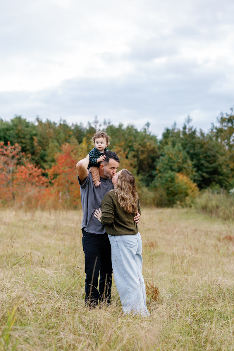 Family laughing with playful toddler surrounded by fall foliage, authentic Wilmington family portraits