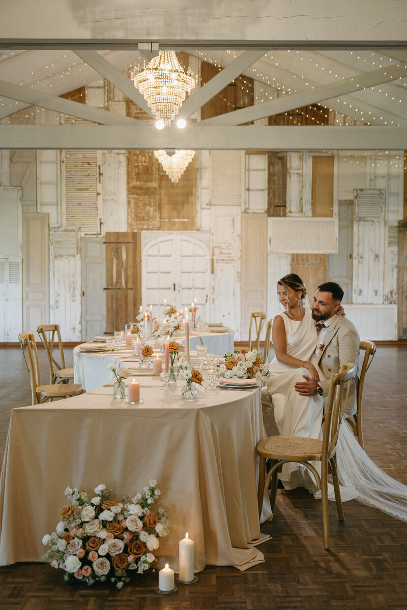 Faustine assise sur les genoux de Dimitri, seuls face à une table  de mariage sinusoidale. Scénographie de mariage imaginée par Nos moments Ensemble, agence évènementielle Nantes Loire Atlantique Vendée