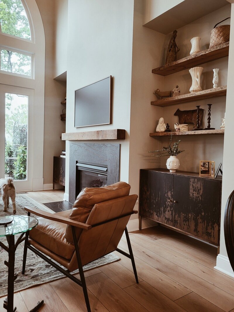 Fireplace with wooden mantle with shot of shelving nooks with artisticlly painted cabinets  that coordinate with the fireplace surround and colors in the living room