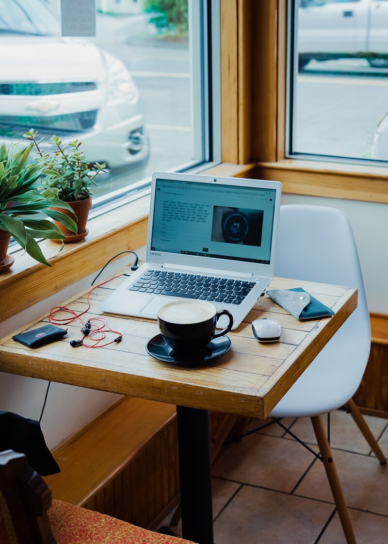 image of laptop and latte in a mug on a wooden table in a bright coffee shop