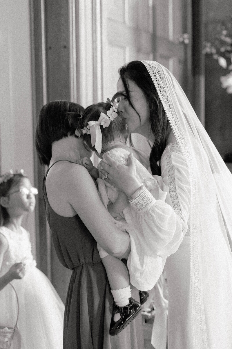 a bride in a lace veil and long sleeves kisses her flower girl daughter at lairmont manor.