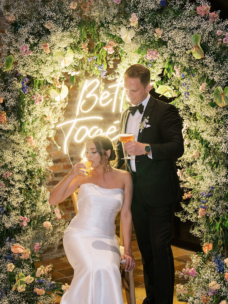 Bride and groom enjoying a cocktail at their floral arch during their wedding reception.