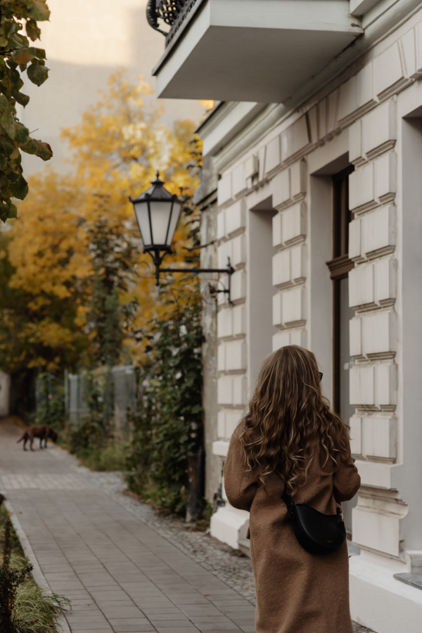 Young woman walking past a stone building with a street lamp toward some  beautiful yellow trees | Brand By Design