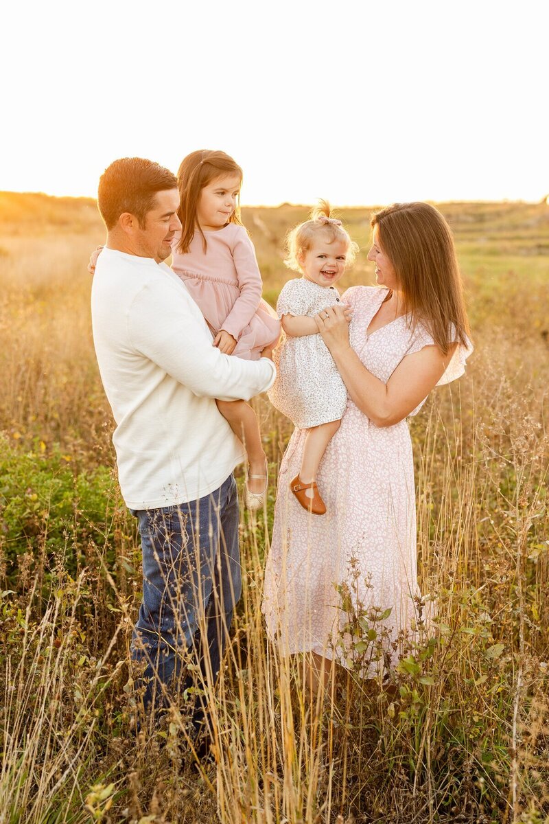 Family smiling at each other in a golden field, taken by minneapolis family photographer Kacey Wyrick Photography