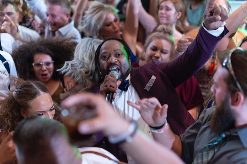 Wedding guests dancing with high energy on the dance floor as the DJ hypes up the crowd.
