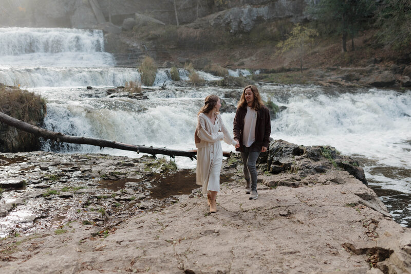Ann and Riley enjoying their colorful fall engagement session while hiking at a state park in Wisconsin by a stunning waterfall