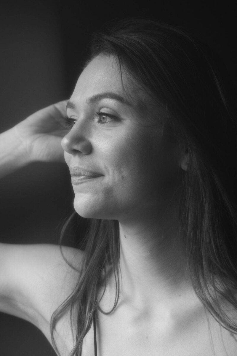 Portrait intimiste d'une jeune femme regardant par la fenêtre en souriant lors de sa séance photo portrait à Lyon