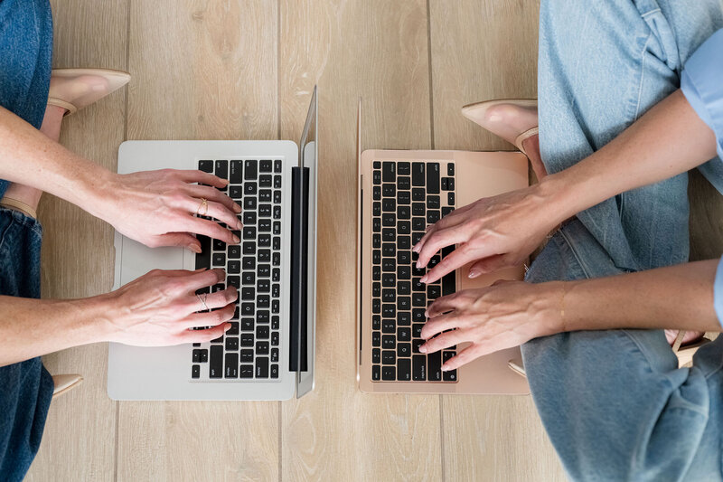 two women typing on laptops on the floor