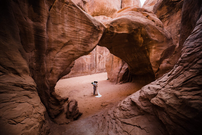 A couple dances under a huge red rock arch.
