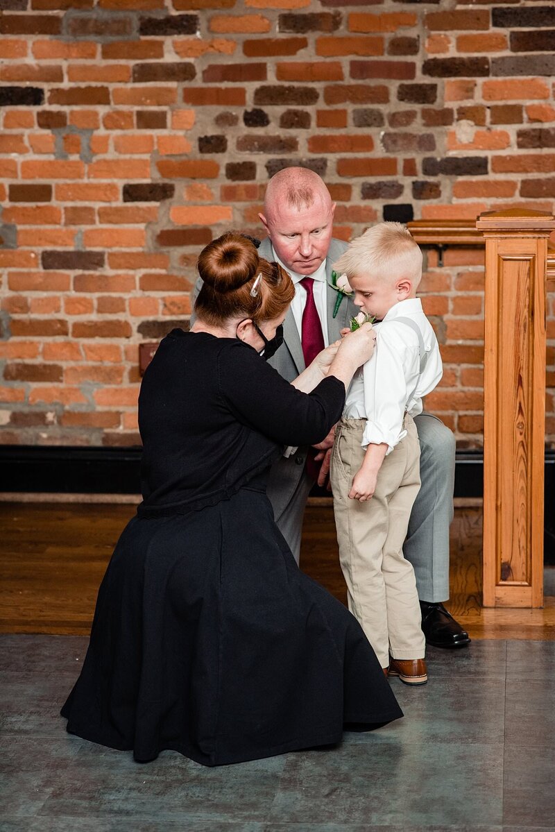 Wedding planner kneeling and pinning the boutonniere onto the ring bearer