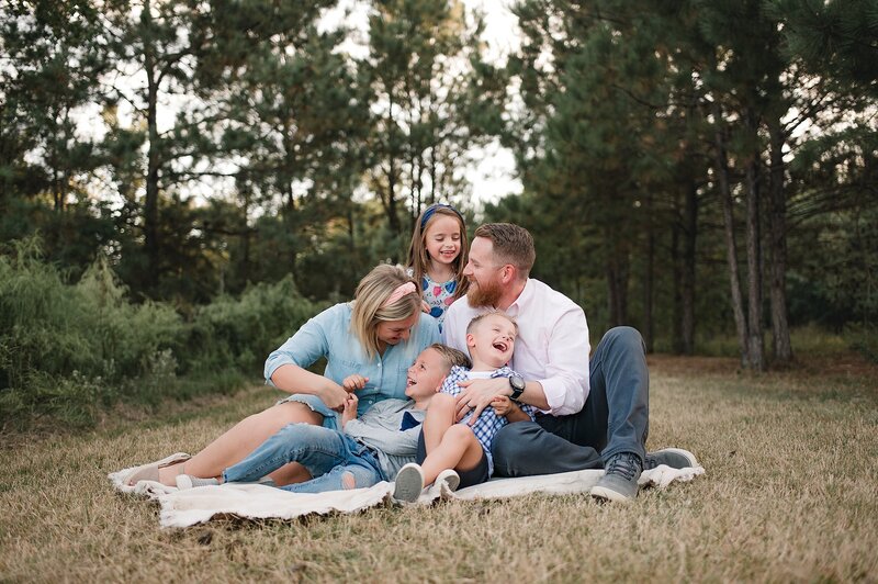 Family of 5 sitting outside laughing and tickling each other by Houston Newborn Photographer