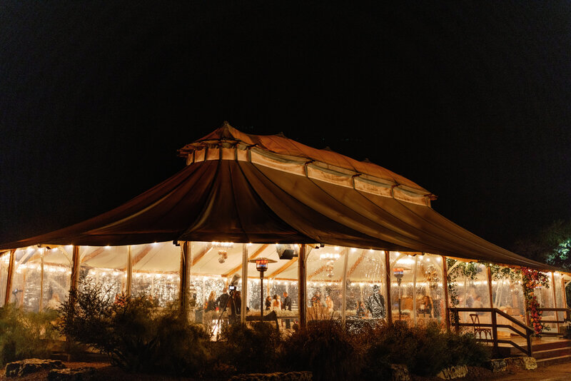 Nighttime wedding reception at Camp Lucy, featuring a warmly lit tent filled with guests celebrating under the Texas sky.
