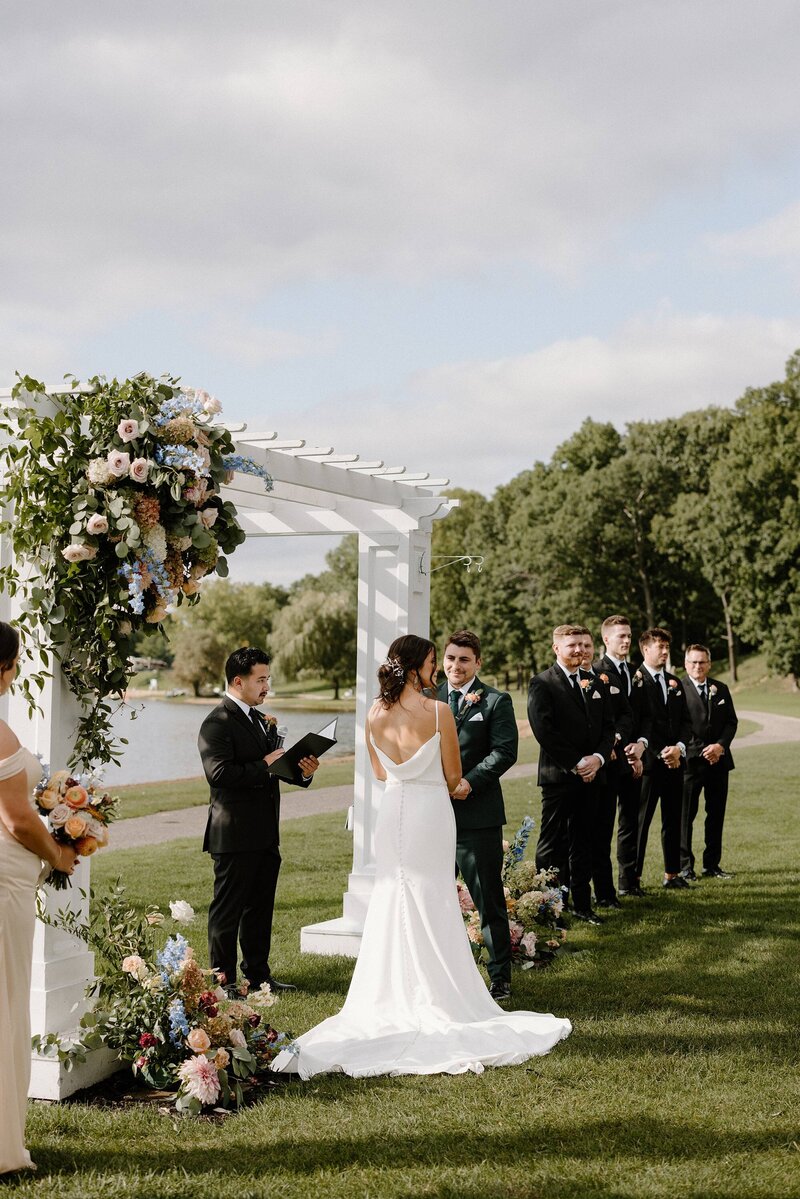 a wedding ceremony along a lake with a white gazebo and trees