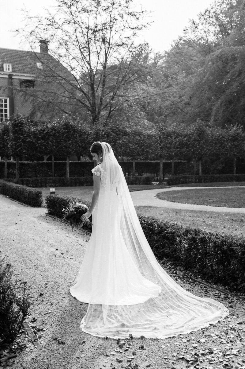 Bruid poseert voor fotograaf met haar rug en met de sluier en jurk mooi uitgelegd bij de Havixhorst