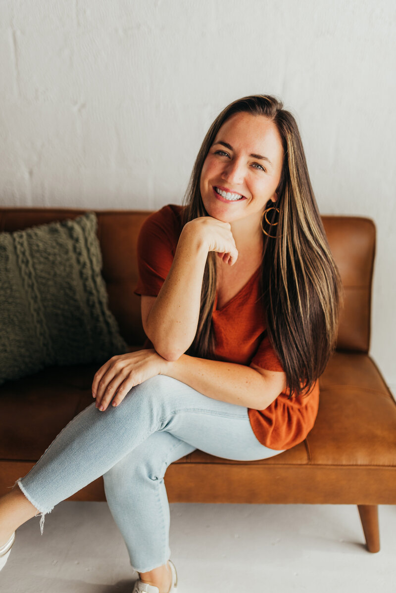 photographer wearing burnt orange top  with long brown hair smiles happily into the camera