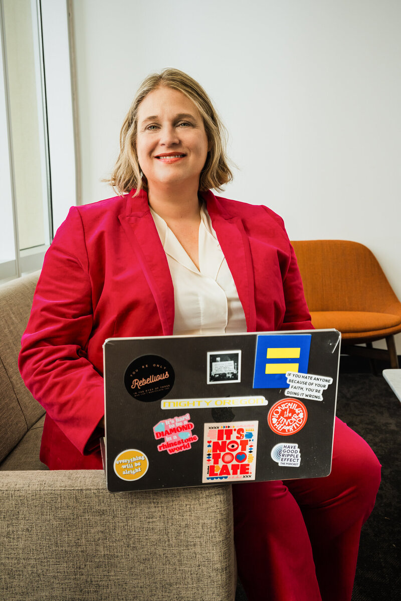 Mya Andersen in a red suit sits with a laptop covered in colorful stickers on their lap, embodying the confidence that comes from Personalized Academic Life Coaching for College Success