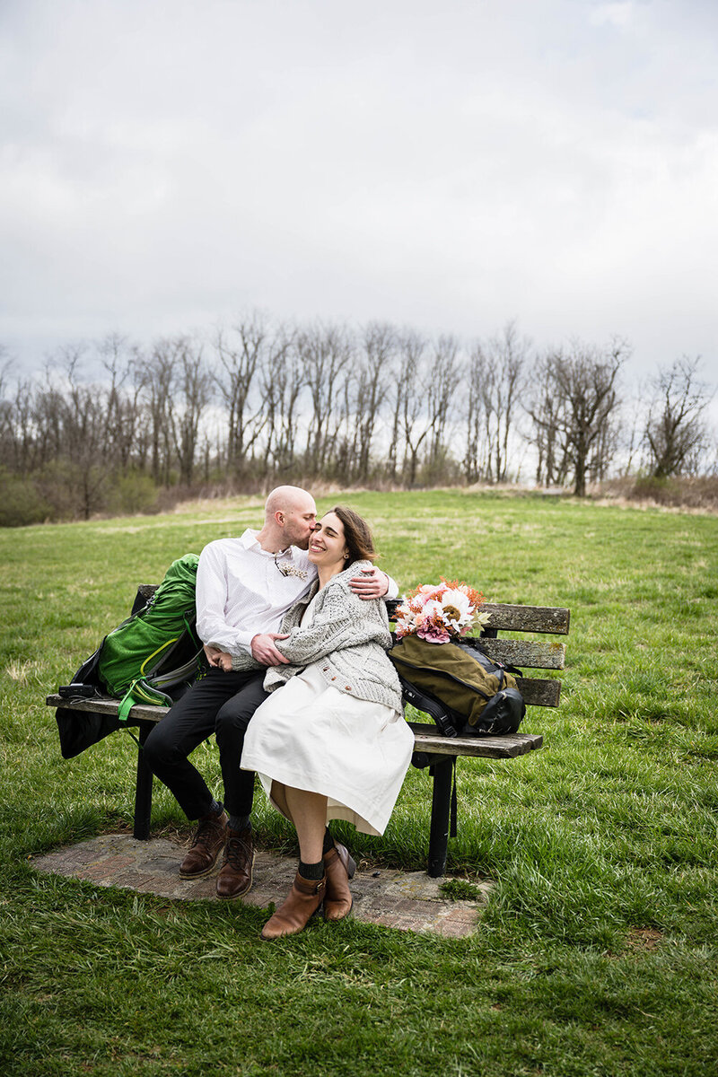 A Virginia elopement photographer stands on a bride at Wasena Park wearing a backpack and holding her camera.