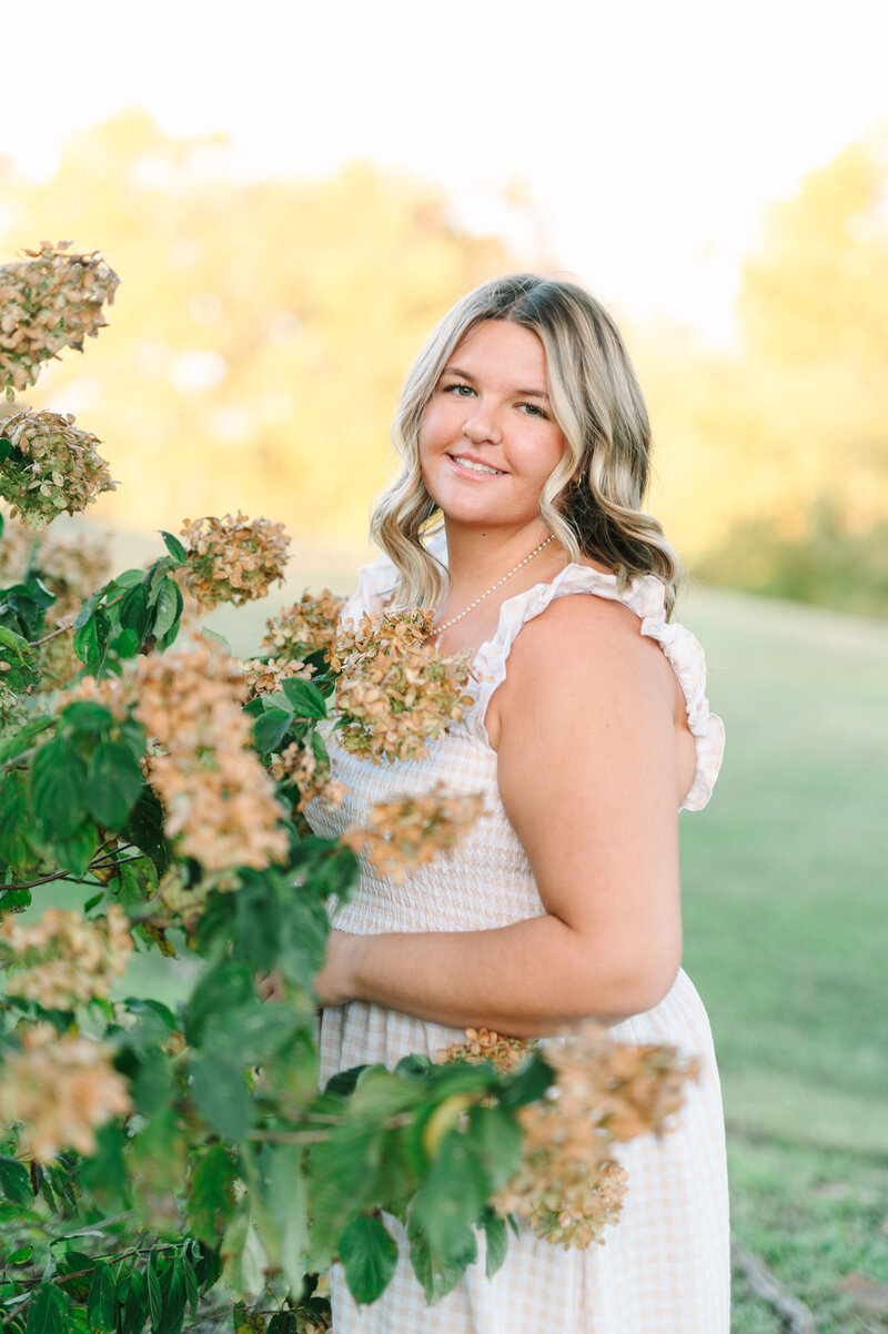 a high school senior girl smiling while standing by a flower bush