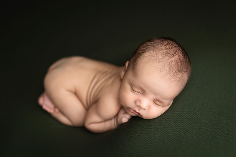 Newborn boy posed on green during his newborn session.
