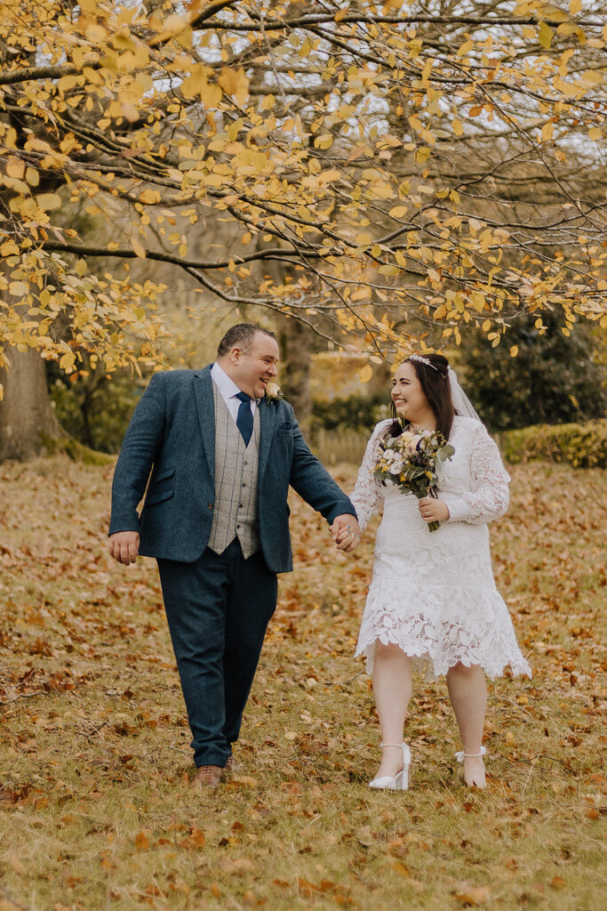 Bride and groom walking through autumn leaves at  Bakewell ceremony and Chatsworth celebration