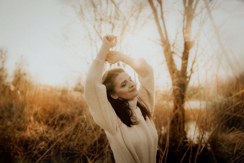 a young woman wearing a beige turtleneck sweater holding her hands up