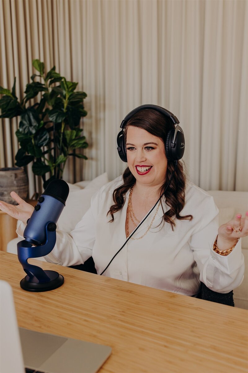 woman speaking smiling in front of podcast yeti mic in white shirt and headphone