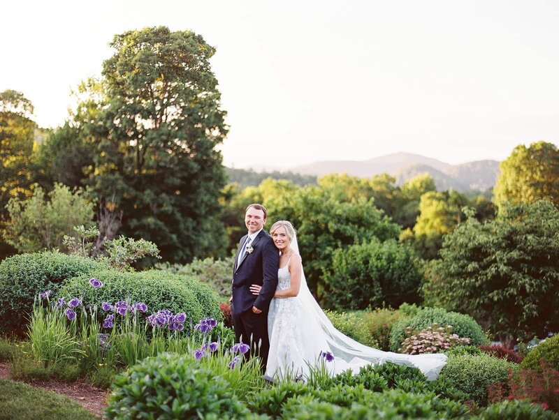 A bride holds her groom while an Asheville Wedding Photographer captures their moment with mountains in the background