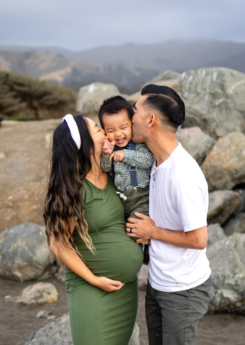 Pregnant couple kisses their smiling toddler in front of scenic rocks — Bay Area Photographer Services - Ellobelle Photography Family Photographer