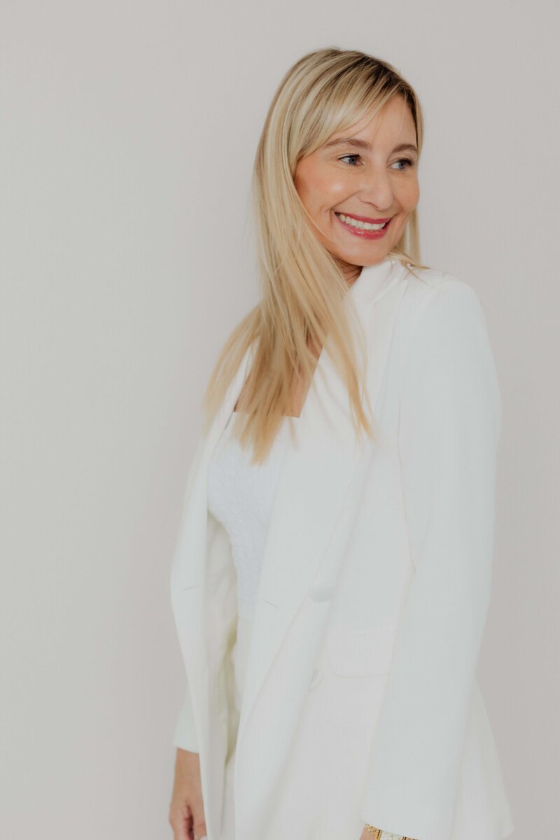 A omen blond women smiling in a white suite.