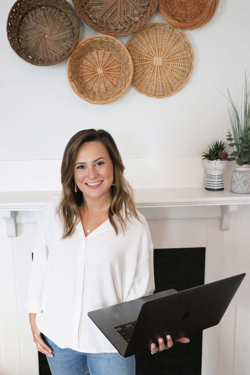 woman holding a laptop while smiling and wearing a white shirt